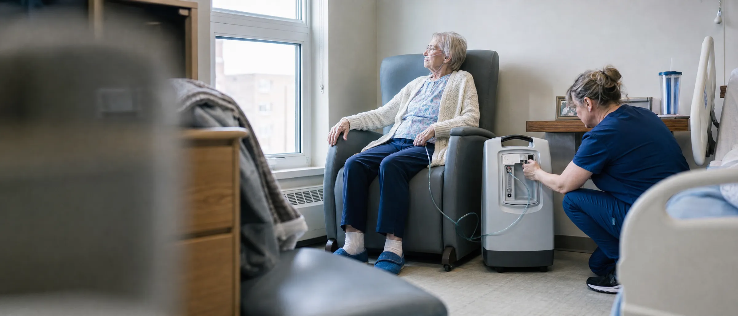A nurse checks an oxygen concentrator beside a resident seated in an armchair