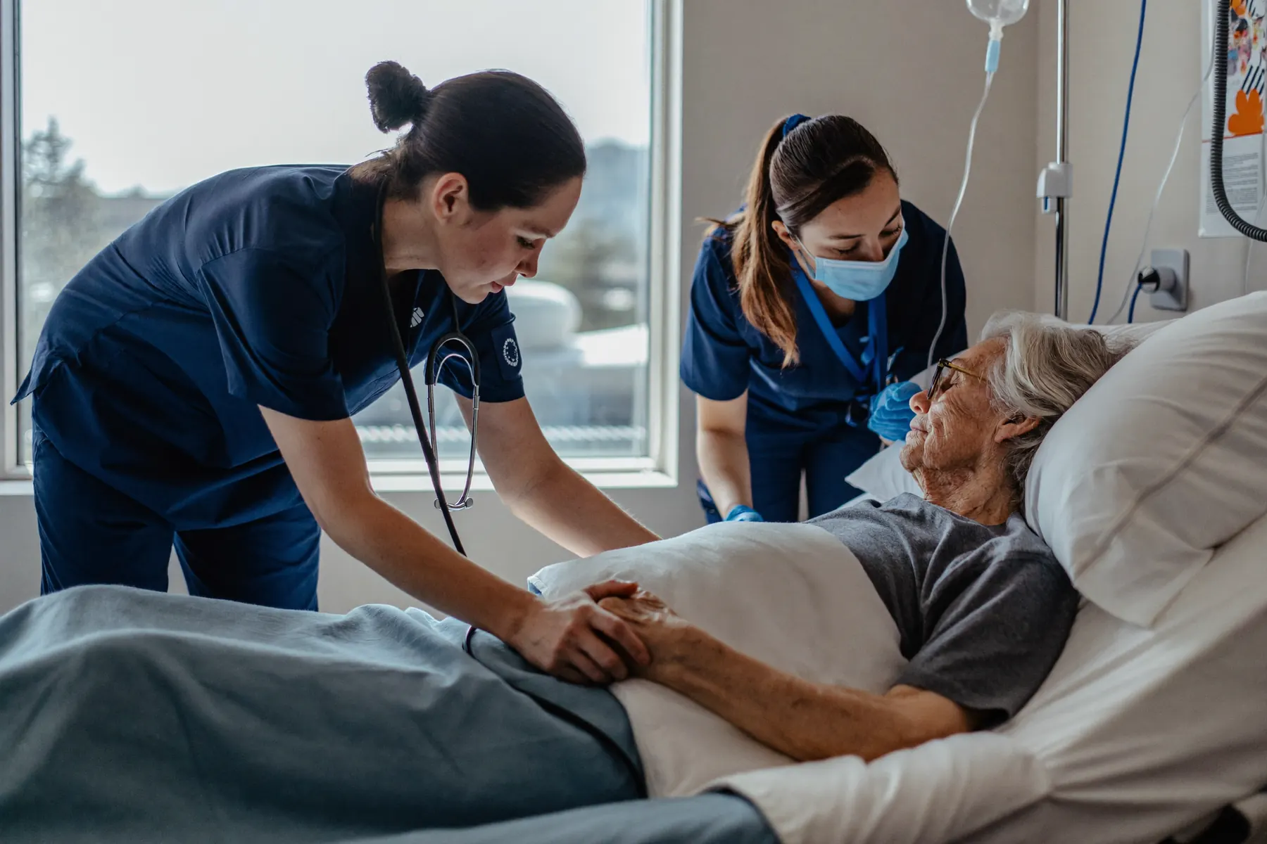 Two nurses caring for an older patient at the bedside