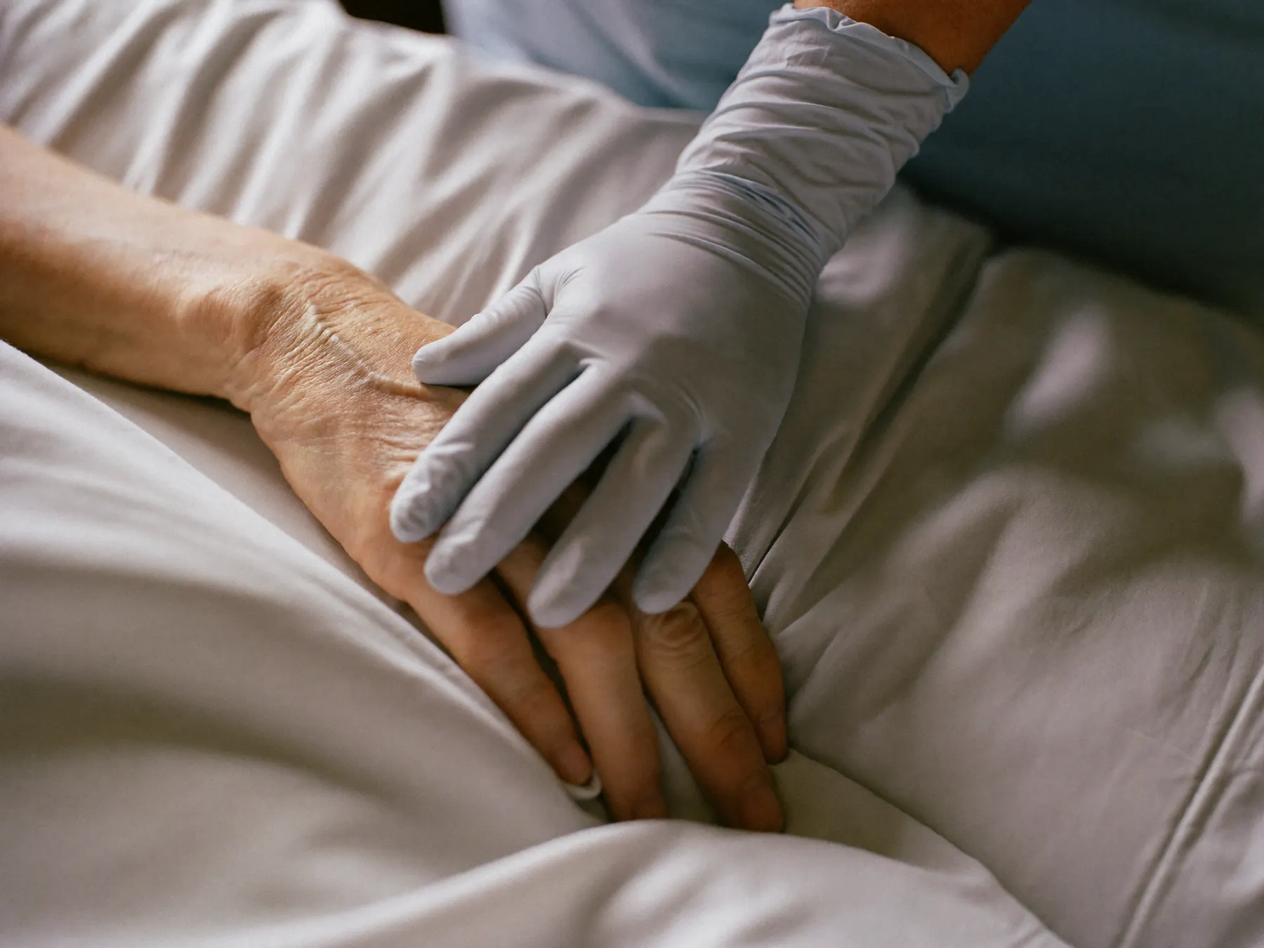 A caregiver's gloved hand resting on an elderly patient's hand