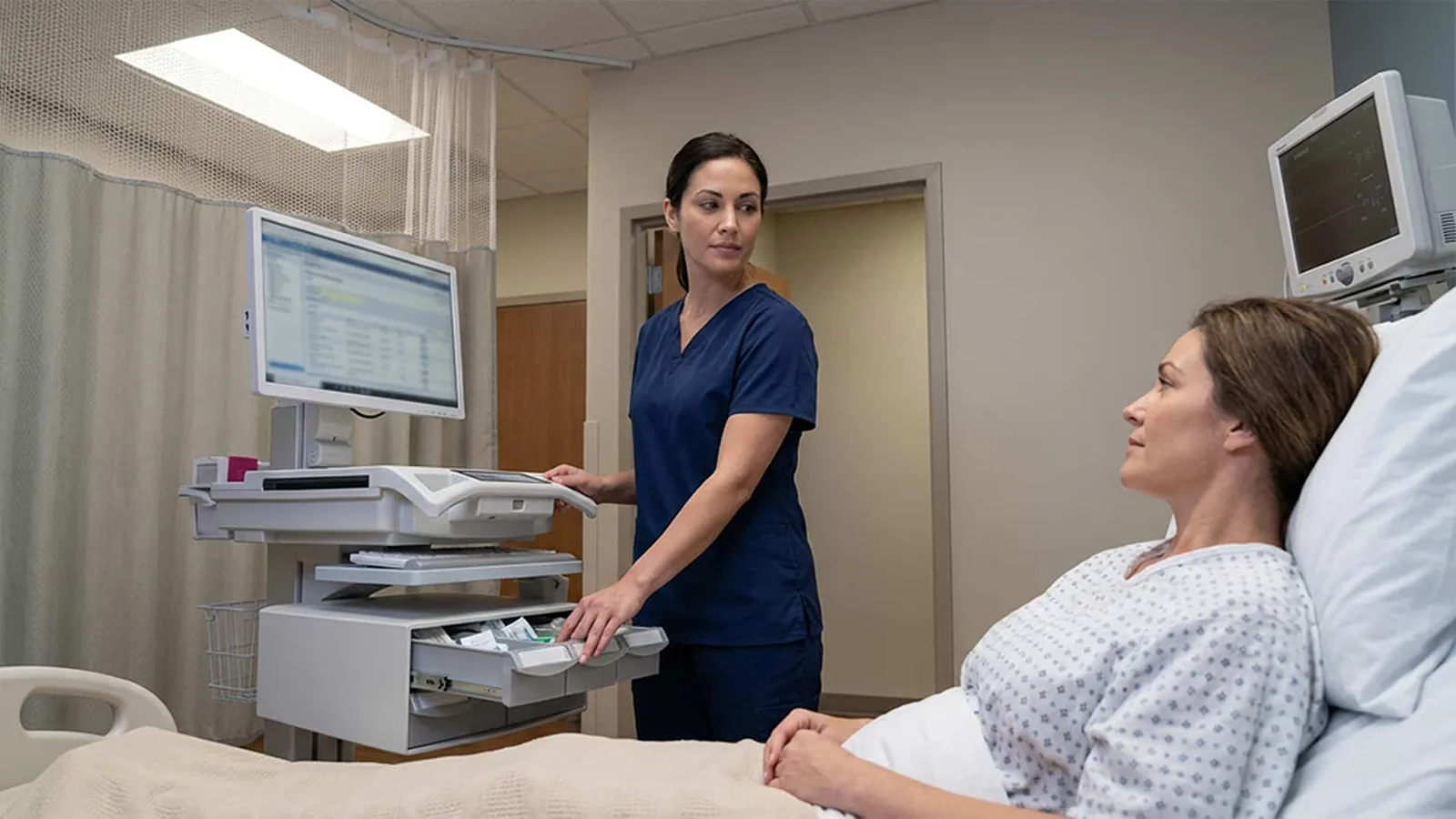 A nurse opening a drawer of a Capsa Trio workstation at a patient’s bedside