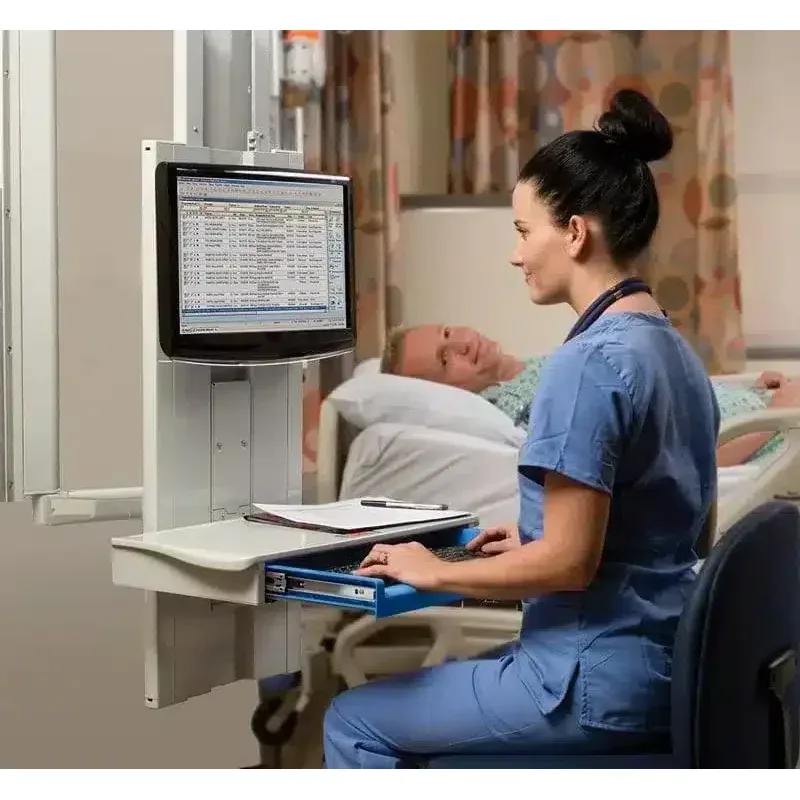 A nurse seated at a Tandem wall arm beside a patient’s bed