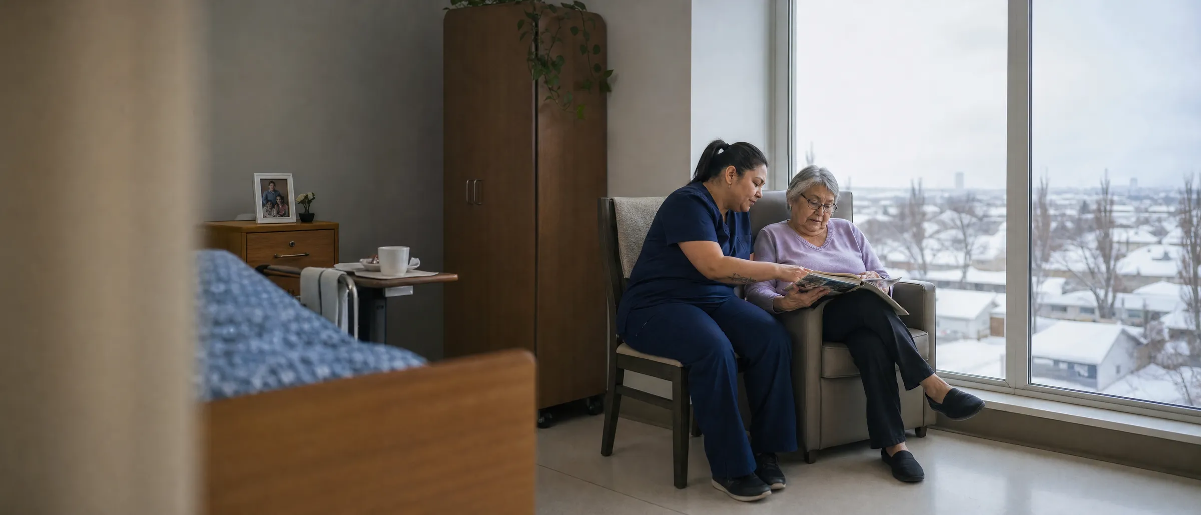 A care aide and a resident looking at a photo album by a window over a snowy Winnipeg neighbourhood